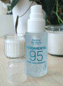 Flacon du Fondamental 95 à l'eau thermale et à l'acide hyaluronique en photo devant des bougies et des plantes